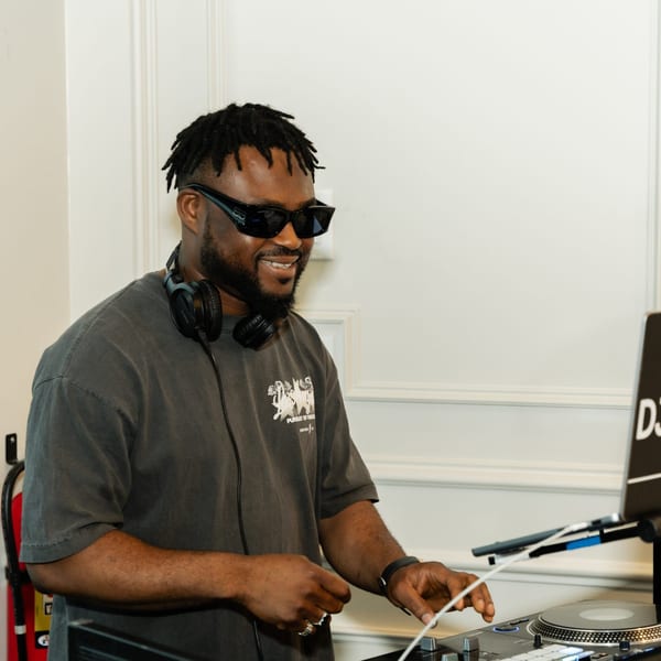A smiling DJ with dreadlocks and sunglasses, wearing headphones, mixing music at Cubana Grille.