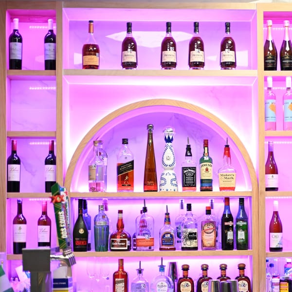 A well-lit bar shelf at Cubana Grille, displaying various liquor bottles with purple backlighting.