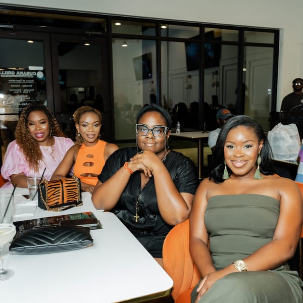 Four women smiling at a table inside Cubana Grille, with drinks and purses on the table.