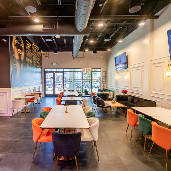Cubana Grille's dining room with colorful chairs, white tables, and a large mural on the left wall.