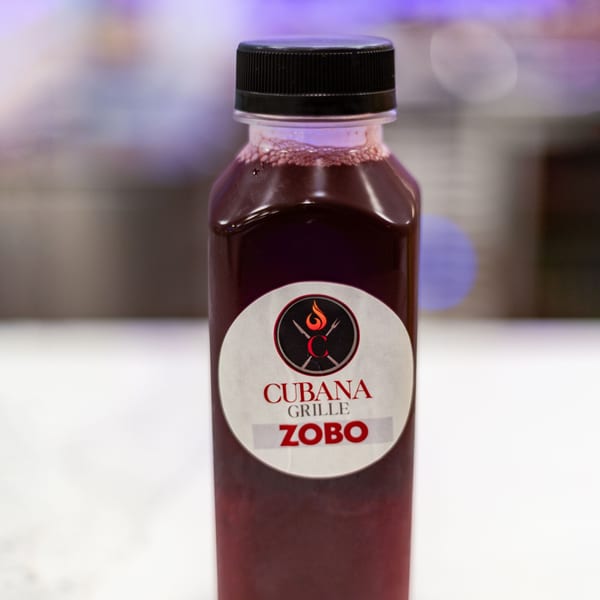 Cubana Grille Zobo drink in a clear bottle with a black cap, against a blurred background.