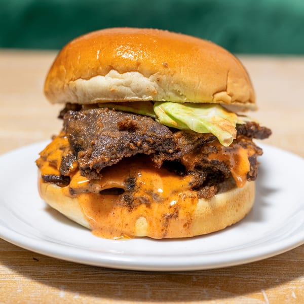 A Cubana Grille burger with dark meat, orange sauce, and green lettuce on a white plate.