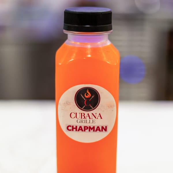 A bottle of bright orange juice with a Cubana Grille label on a white surface.