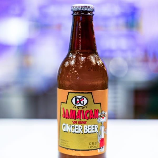 A cold bottle of DG Genuine Jamaican Ginger Beer with condensation, against a blurred background.